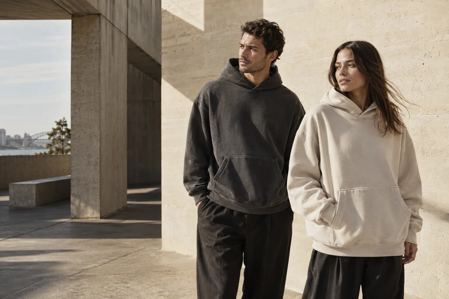 Two models in Ink and Bone hoodies against sunlit limestone